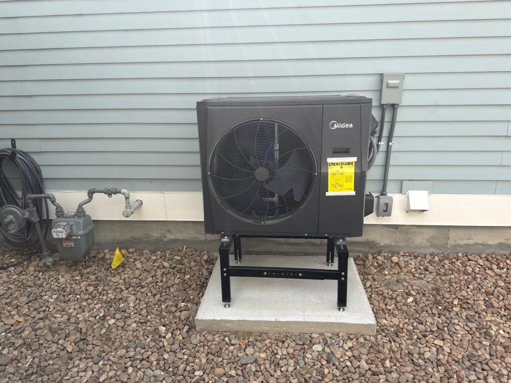 New Midea outdoor heat pump unit installed at Robert Germain's home, mounted on a black stand on a fresh concrete pad with the yellow EnergyGuide label still attached.