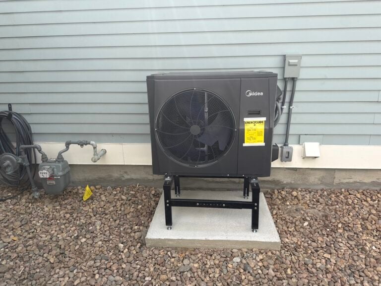 New Midea outdoor heat pump unit installed at Robert Germain's home, mounted on a black stand on a fresh concrete pad with the yellow EnergyGuide label still attached.