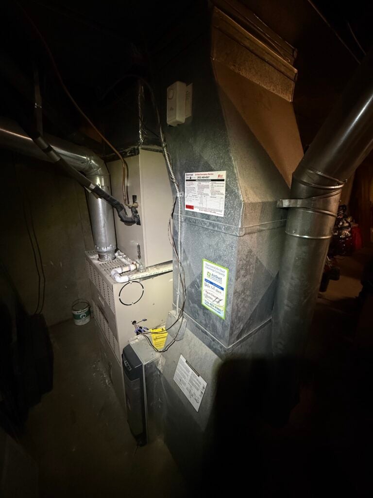 Existing furnace and sheet-metal ductwork in David's dimly lit basement mechanical room before the install.