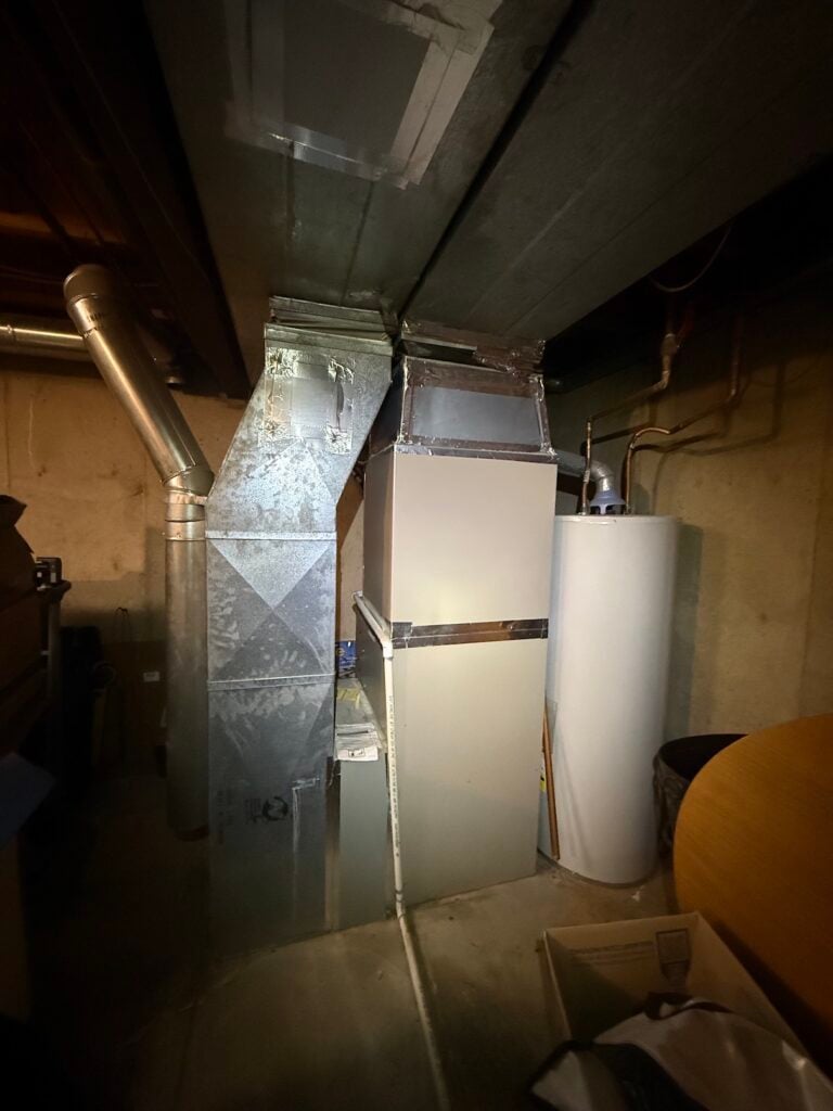Existing furnace and gas water heater in David's basement before the install, with supply and return ductwork running to the ceiling.