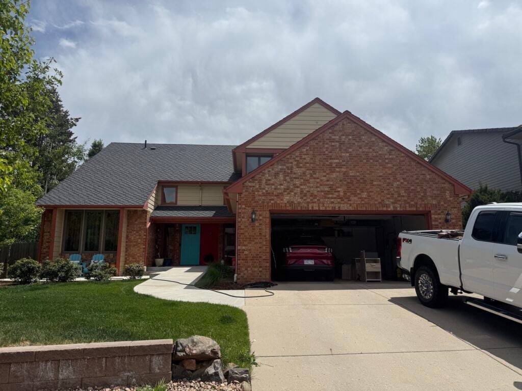 Front exterior of David's brick and tan two-story home before the install, with an open two-car garage and a work truck parked in the driveway.