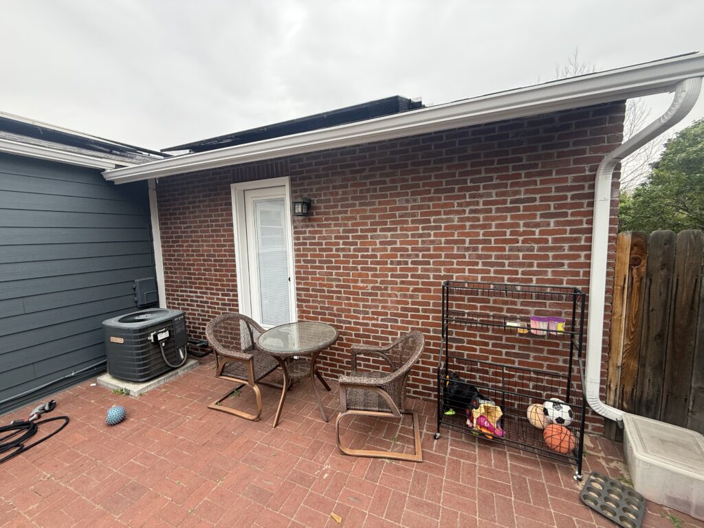 Old outdoor air conditioner condenser on a concrete pad beside a brick home's back patio in Denver, before heat pump installation