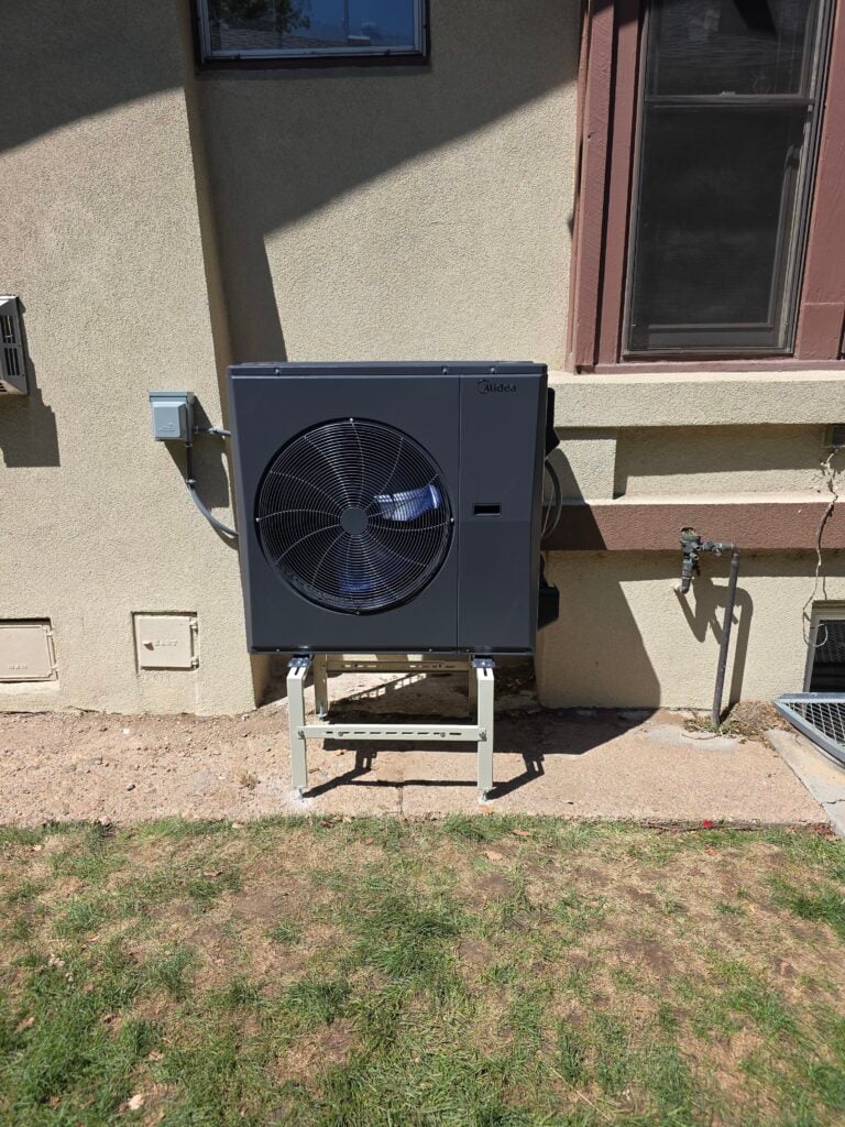 New Midea outdoor heat pump condenser unit installed on a stand beside a stucco home"
