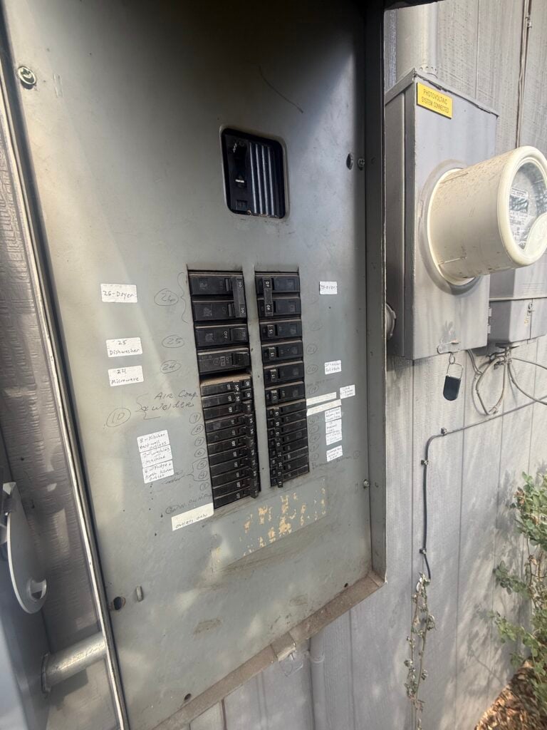 Existing electrical panel with handwritten labels and connected solar system meter before heat pump installation