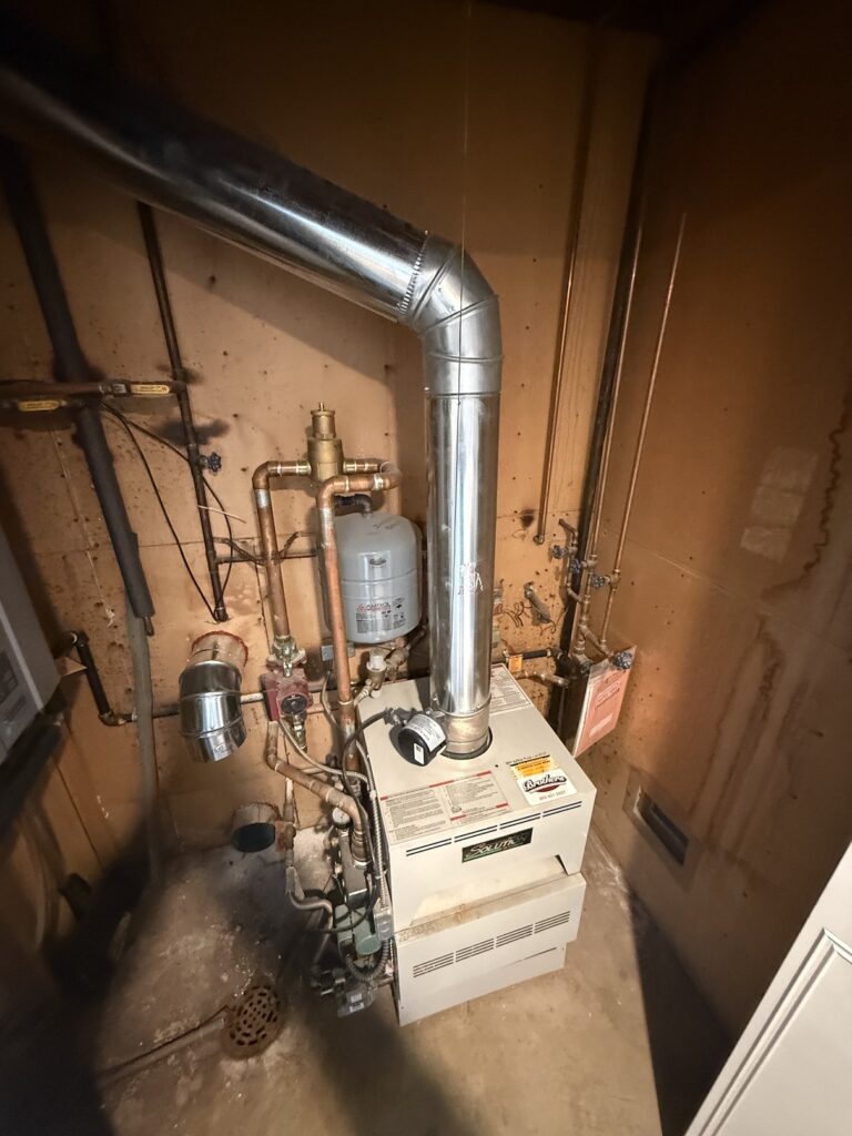 Old gas boiler with flue and copper piping in a basement before heat pump replacement