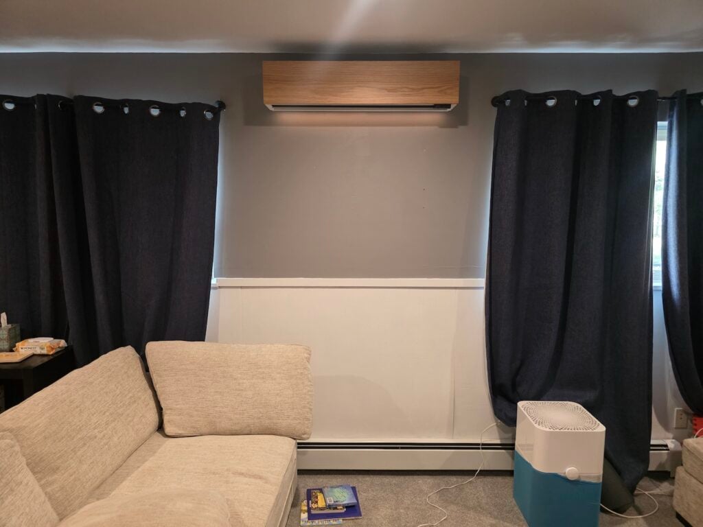 Wood-finish Quilt indoor heat pump unit mounted on a living room wall above wainscoting