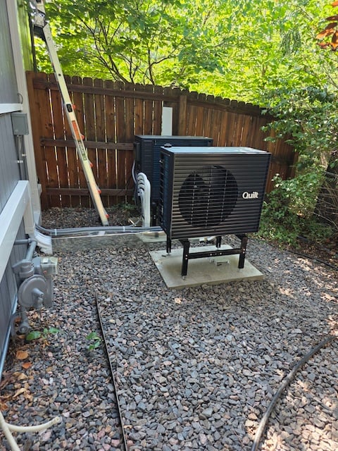 Two black Quilt outdoor heat pump units installed on a concrete pad in a side yard