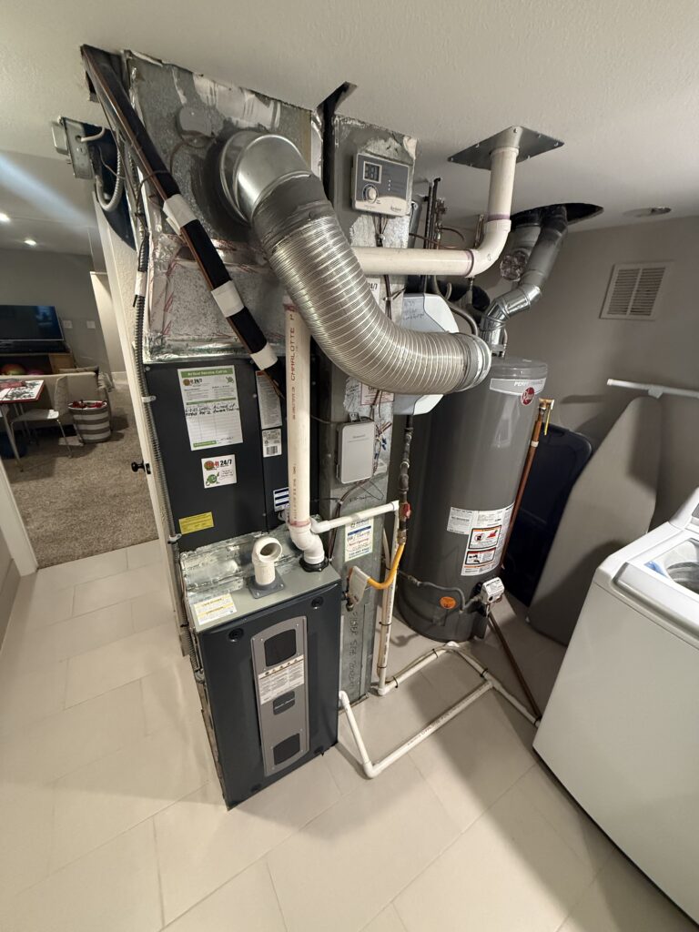 Existing gas furnace, ductwork, and water heater in a Denver basement utility area before heat pump conversion