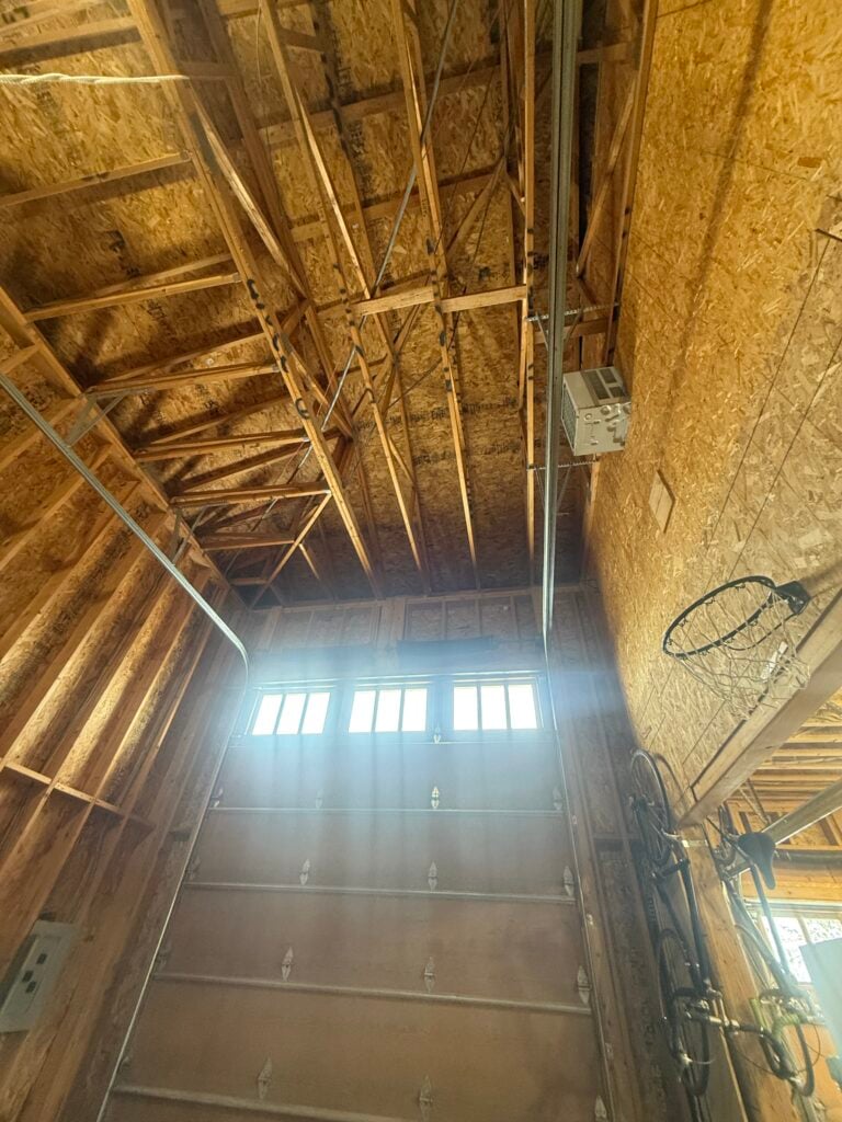 Tall garage bay with exposed framing and an old mounted wall heater before heat pump installation in Lone Tree, CO