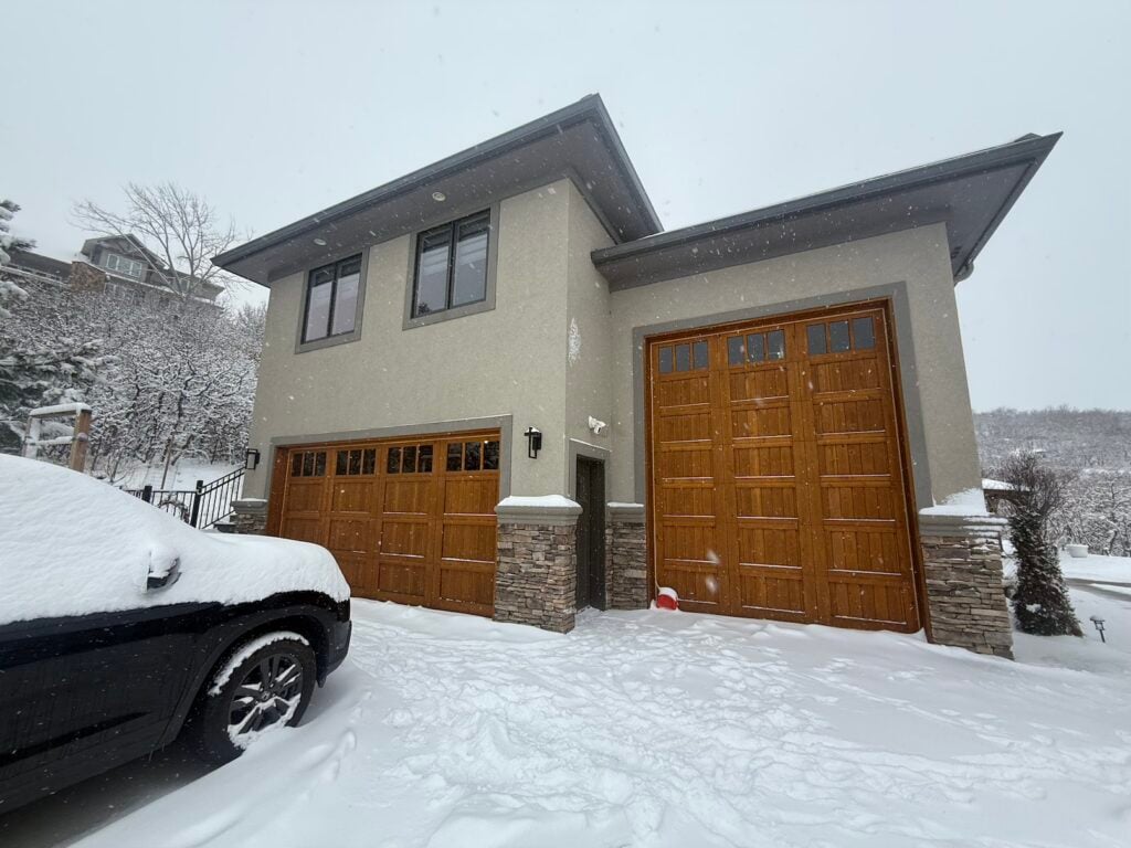 Exterior of a stucco Lone Tree, CO home with wood garage doors in the snow, site of a multi-zone heat pump install