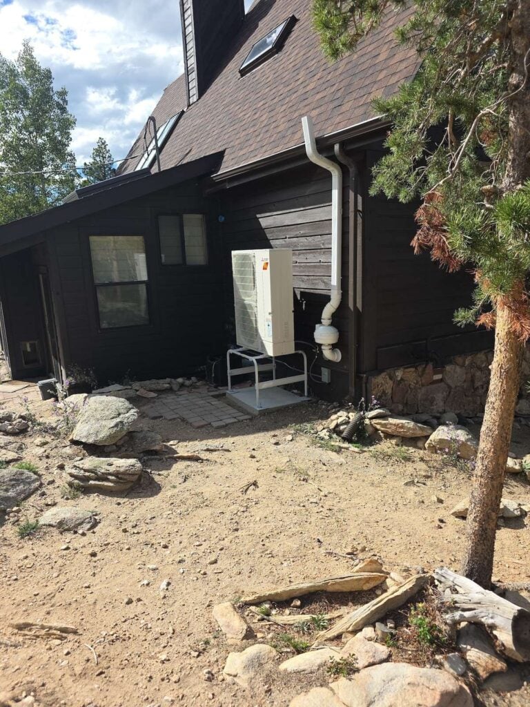 A Mitsubishi heat pump condenser elevated and installed at a Golden, CO mountain wood home.